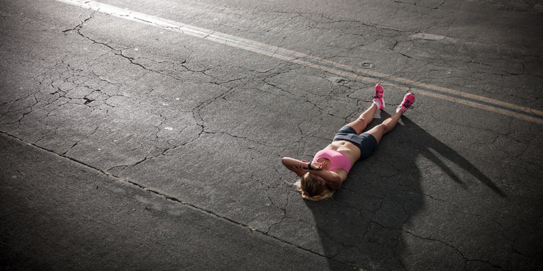 Joggerin liegt erschöpft auf dem Teer, © R_Michael_Svoboda_via_Canva