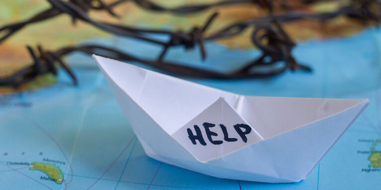 Papierschiff auf Landkarte mit der Aufschrift HELP , © gettyimages/AntonChalakov