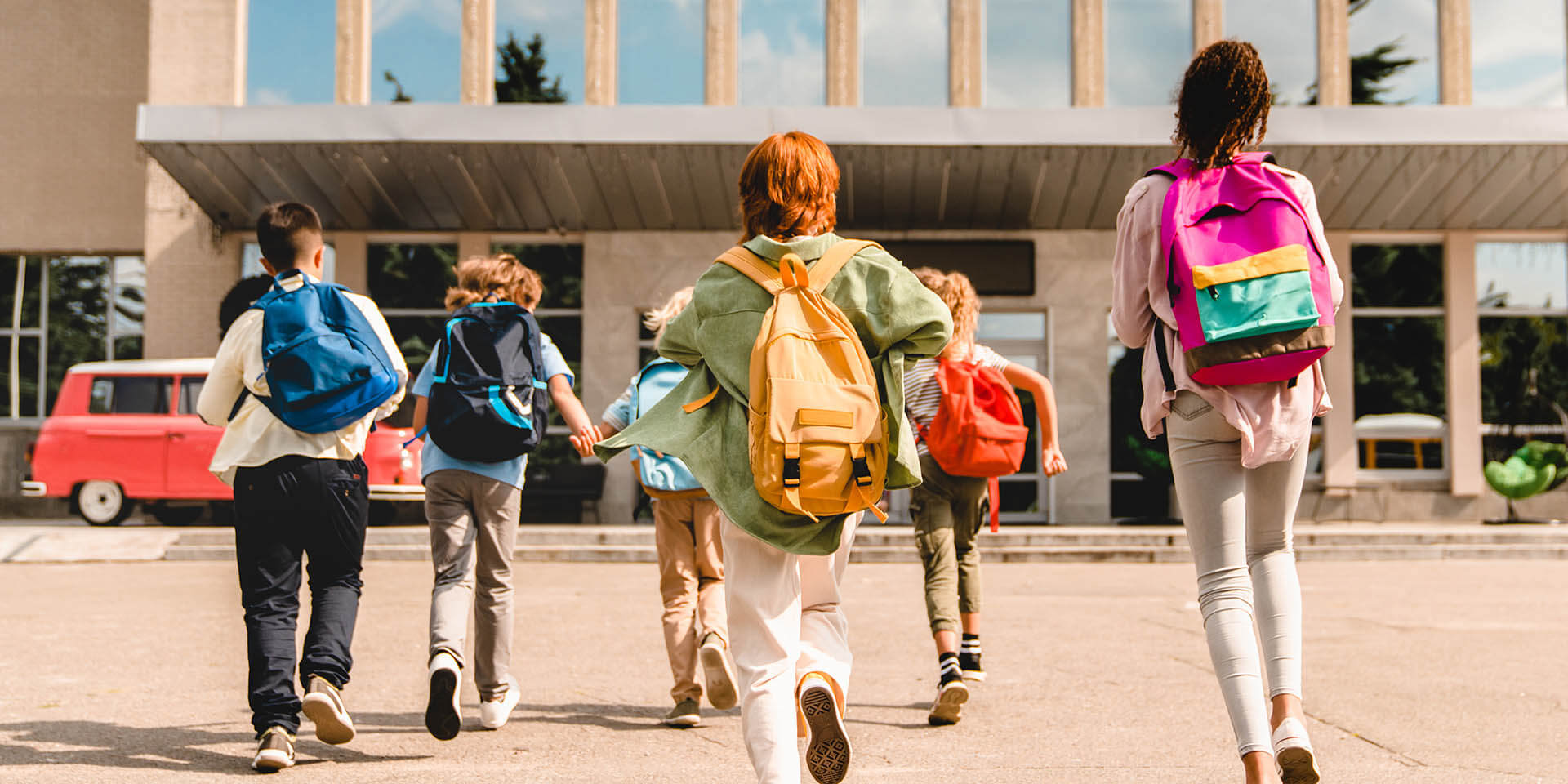 Schülerinnen und Schüler gehen auf ein Schulgebäude zu